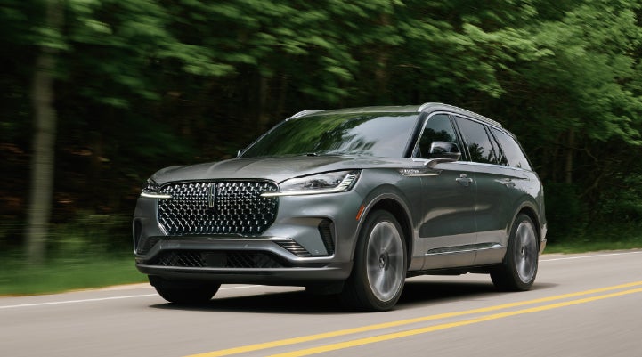 A 2027 Lincoln Aviator® SUV is being driven down a road lined with trees. | Lincoln North Miami in North Miami FL