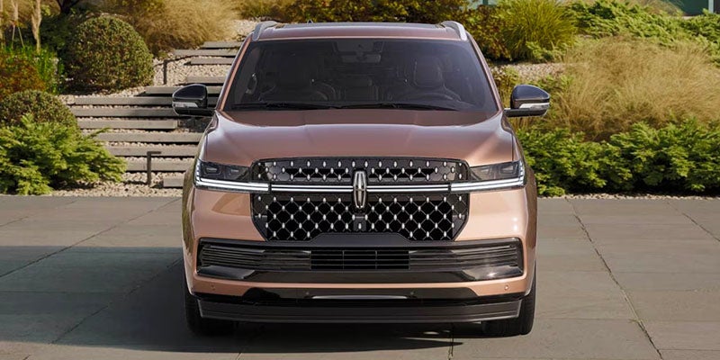 Front view of a bronze Lincoln SUV with a large, intricate grille parked on a paved surface.