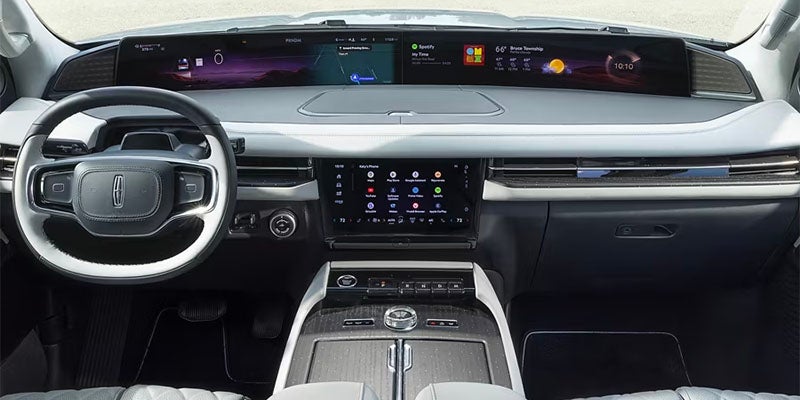 Lincoln vehicle interior with a wide dashboard screen, large central touchscreen, steering wheel, and light gray and dark gray accents.