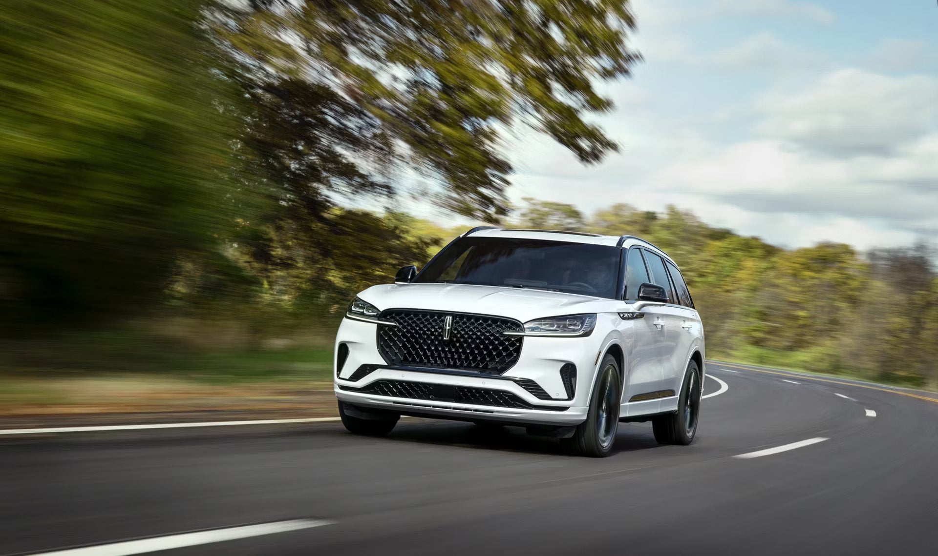 White Lincoln Aviator SUV driving on a winding road with motion-blurred trees in the background.